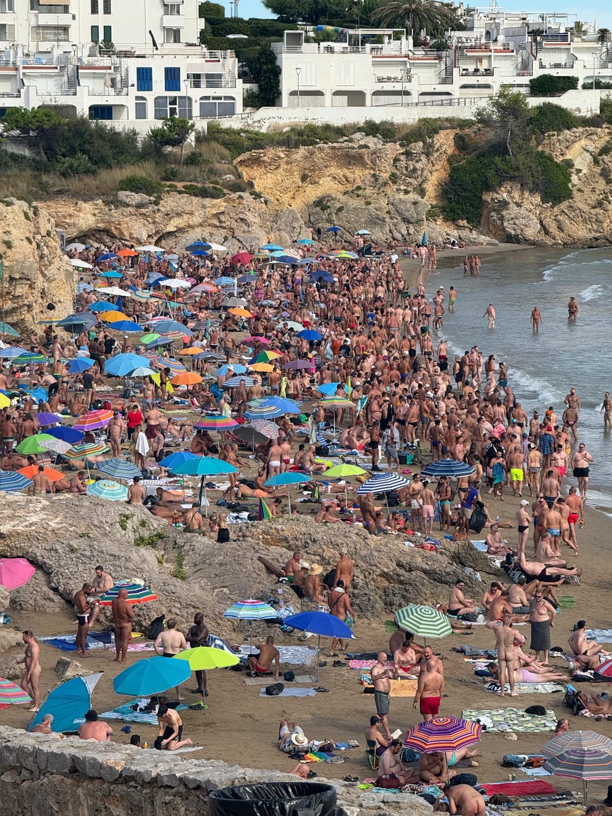 Balmins Beach (the gay bear nude beach) packed with bears and colorful umbrellas during Bears Sitges Week