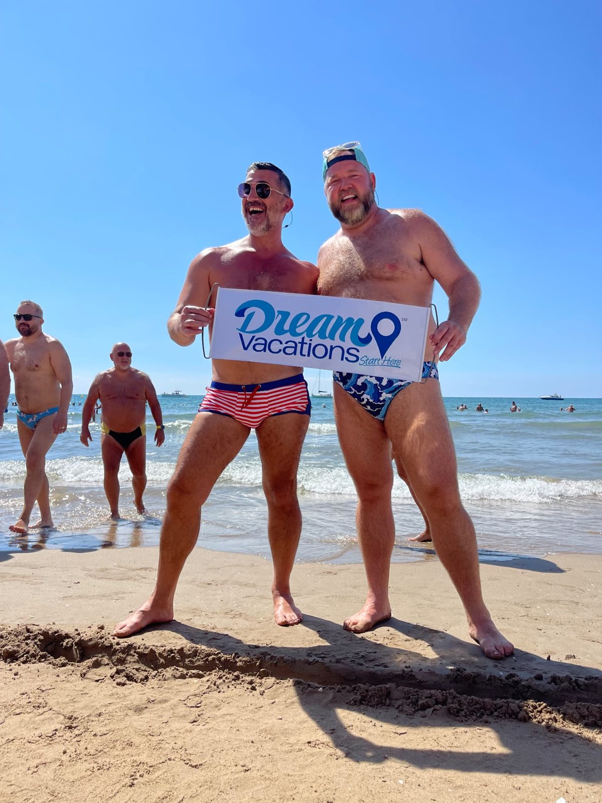 Aram and a friend holding a Dream Vacations banner on the beach in Sitges