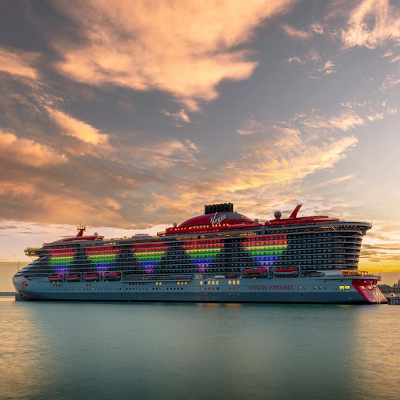 Virgin Voyages ship lit with rainbow Pride colors at sunset in port