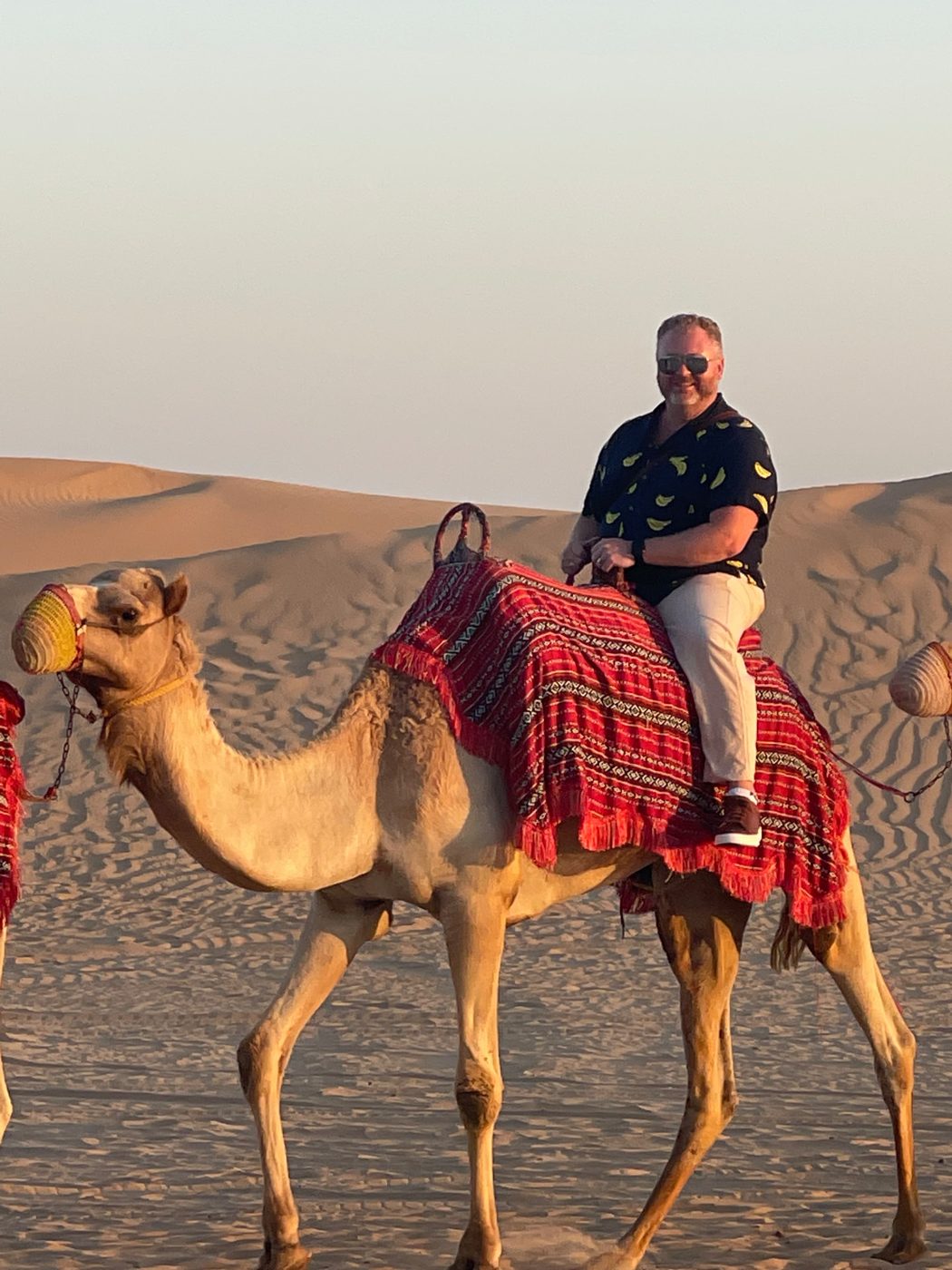 Matthew smiling on a camel ride across the desert dunes