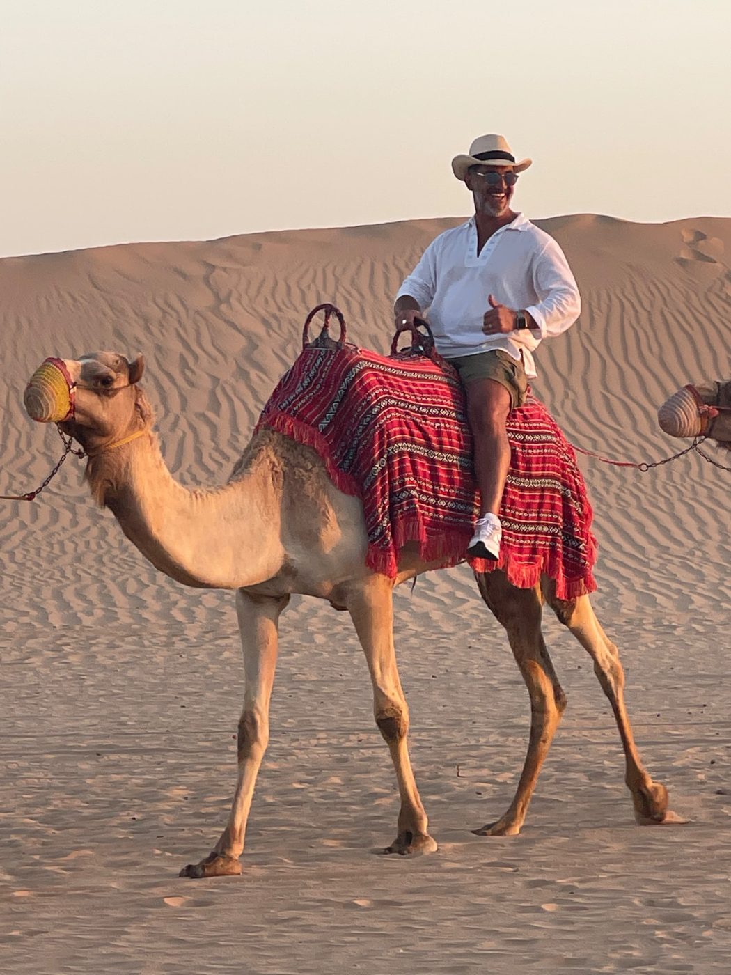 Traveler in a straw hat giving a thumbs up from a camel